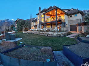Back of property featuring stone siding, a garage, stucco siding, a mountain view, and a yard
