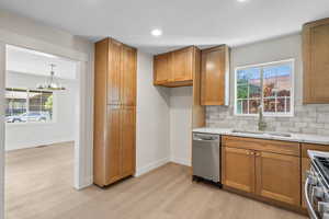 Kitchen featuring appliances with stainless steel finishes, a sink, brown cabinets, light wood finished floors, and light countertops