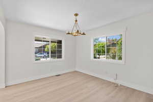 Unfurnished room with plenty of natural light, a chandelier, wood finished floors, and baseboards