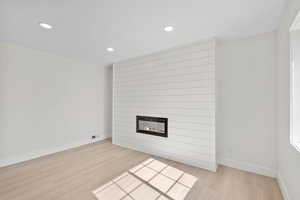 Unfurnished living room featuring light wood finished floors, a large fireplace, recessed lighting, and baseboards