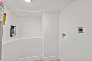 Laundry area with hookup for a washing machine, electric dryer hookup, light wood-style floors, a textured ceiling, and baseboards