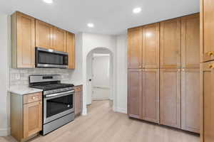 Kitchen with appliances with stainless steel finishes, light wood-style floors, arched walkways, decorative backsplash, and recessed lighting