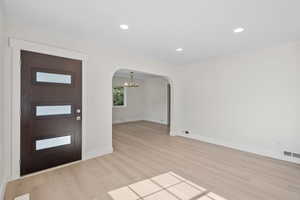 Entrance foyer featuring arched walkways, light wood finished floors, baseboards, a chandelier, and recessed lighting