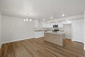 Kitchen featuring white cabinetry, a center island, a chandelier, decorative light fixtures, and stainless steel appliances