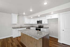 Kitchen with stainless steel appliances, a center island, white cabinets, light stone countertops, and dark wood finished floors