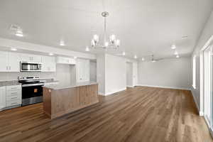 Kitchen featuring appliances with stainless steel finishes, white cabinetry, decorative light fixtures, a kitchen island, and light stone counters