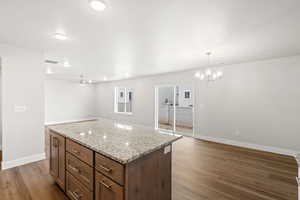 Kitchen featuring open floor plan, light wood-type flooring, a kitchen island, light stone counters, and a textured ceiling