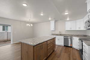 Kitchen featuring a kitchen island, light stone counters, white cabinets, appliances with stainless steel finishes, and dark wood-style floors