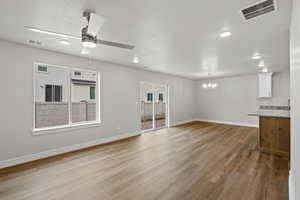 Unfurnished living room featuring a ceiling fan, a textured ceiling, light wood finished floors, and a chandelier