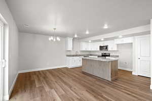 Kitchen featuring white cabinets, a chandelier, pendant lighting, appliances with stainless steel finishes, and a kitchen island