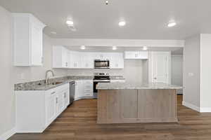 Kitchen featuring light stone countertops, appliances with stainless steel finishes, white cabinetry, a center island, and dark wood finished floors