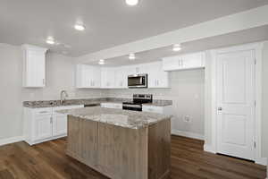 Kitchen featuring white cabinetry, appliances with stainless steel finishes, light stone countertops, a kitchen island, and a textured ceiling