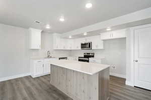 Kitchen with appliances with stainless steel finishes, a kitchen island, white cabinets, light stone countertops, and dark wood-style floors