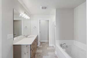 Full bathroom with vanity, a textured ceiling, a garden tub, and light stone finish flooring