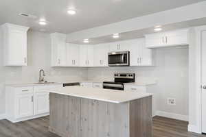 Kitchen featuring appliances with stainless steel finishes, a kitchen island, dark wood-style flooring, white cabinetry, and recessed lighting