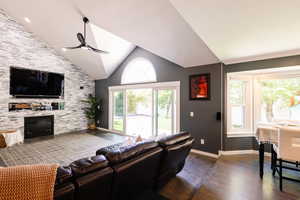 Living area with a ceiling fan, dark wood finished floors, a stone fireplace, baseboards, and high vaulted ceiling