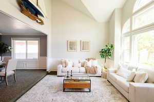 Carpeted living area with a decorative wall, a high ceiling, and wainscoting