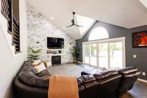 Living area with a ceiling fan, a stone fireplace, high vaulted ceiling, and baseboards
