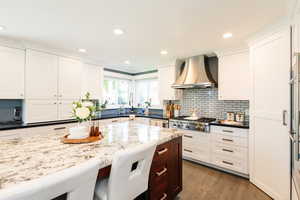 Kitchen featuring wall chimney range hood, stainless steel gas cooktop, a sink, white cabinetry, and dark wood-style flooring