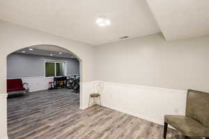 Living area with wood finished floors, arched walkways, a textured ceiling, baseboards, and recessed lighting