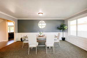 Dining area with carpet, crown molding, wainscoting, and a decorative wall