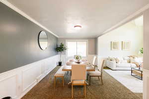 Dining room with a decorative wall, ornamental molding, carpet, and wainscoting