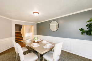 Dining area featuring carpet floors, wainscoting, ornamental molding, a decorative wall, and stairway