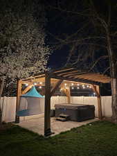 Patio at twilight with a hot tub and a pergola