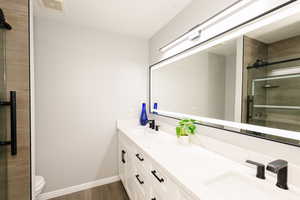 Bathroom featuring a shower stall, wood finished floors, double vanity, baseboards, and toilet