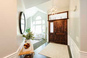 Foyer with a chandelier, vaulted ceiling, wainscoting, a decorative wall, and crown molding