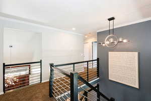 Hallway with an upstairs landing, ornamental molding, a chandelier, carpet flooring, and baseboards