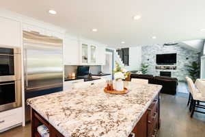 Kitchen with appliances with stainless steel finishes, dark wood-type flooring, light stone counters, glass insert cabinets, and white cabinets
