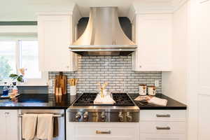 Kitchen with island exhaust hood, stainless steel gas stovetop, dark countertops, backsplash, and white cabinets