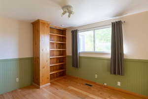Unfurnished bedroom with a wainscoted wall and wood finished floors