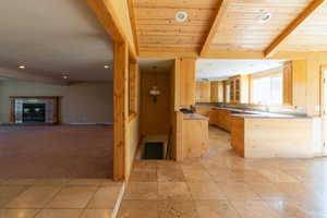 Kitchen with beamed ceiling, open floor plan, a sink, glass insert cabinets, and light brown cabinetry