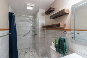 Full bath featuring tiled shower, tile walls, toilet, and wainscoting