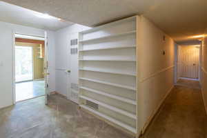 Hall featuring a textured ceiling, carpet flooring, and baseboards