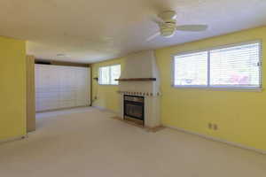 Unfurnished living room featuring a fireplace, light colored carpet, a ceiling fan, baseboards, and a textured ceiling