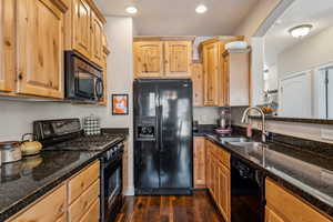 Kitchen with black appliances, dark wood flooring, dark stone counters, and recessed lighting