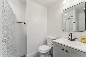 Basement bathroom featuring toilet, baseboards, vanity, and curtained shower