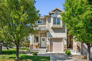 View of property featuring a garage, stone siding, driveway, and a front yard
