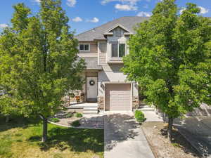 View of front of property featuring an attached garage, concrete driveway, a shingled roof and a front lawn