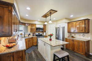Kitchen with appliances with stainless steel finishes, a sink, a kitchen island, dark wood-type flooring, and decorative backsplash