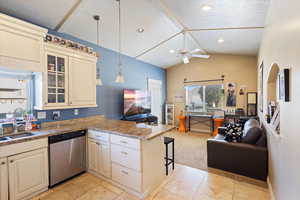 Kitchen with open floor plan, light carpet, dishwasher, a breakfast bar area, and light stone countertops