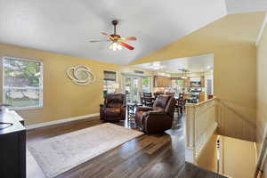 Living area with lofted ceiling, plenty of natural light, a ceiling fan, dark wood-style floors, and baseboards