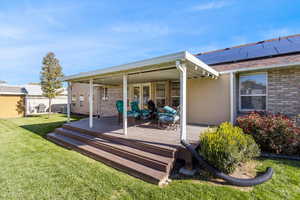 Rear view of house featuring a yard, roof mounted solar panels, and a deck