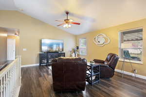 Living room with ceiling fan, vaulted ceiling, dark wood-type flooring, and baseboards