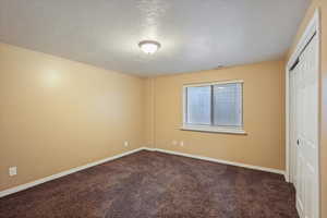 Unfurnished bedroom with dark colored carpet, baseboards, a closet, and a textured ceiling