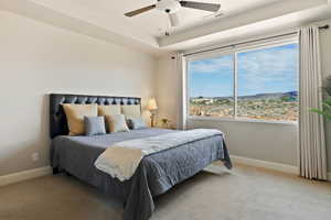 Carpeted bedroom with baseboards, ceiling fan, and a tray ceiling