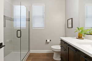 Full bath featuring a shower stall, wood finished floors, vanity, toilet, and baseboards